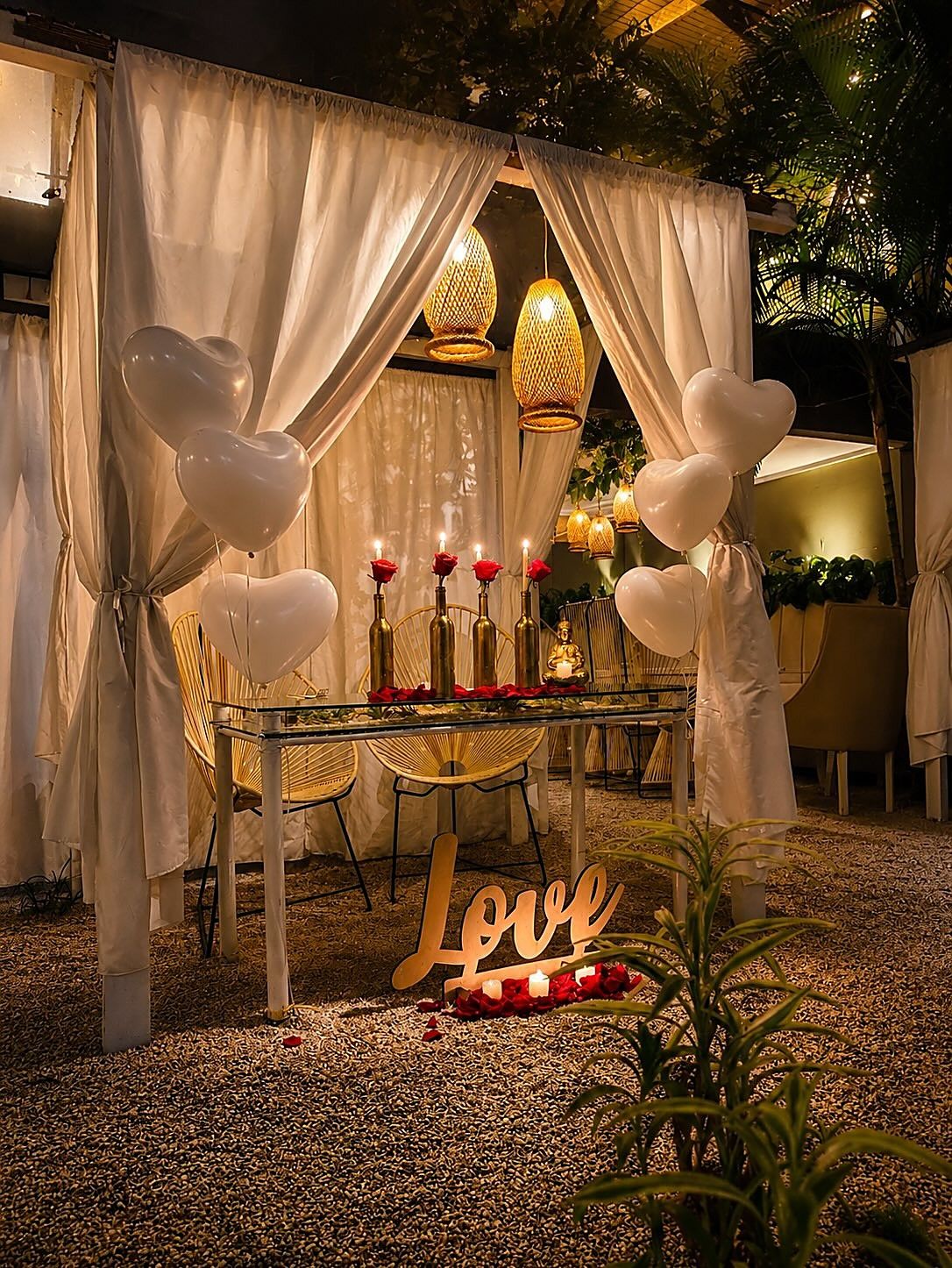Cabaña de Mystic decorada para una cena romántica, con globos blancos, velas, pétalos y un letrero que dice Love